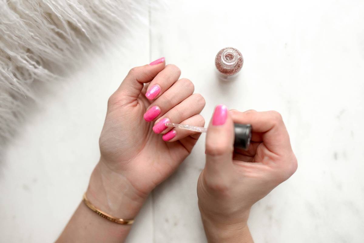 close-up of a hand showing healthy pink nails with a thin, clear nail shield layer applied evenly under rose-pink polish